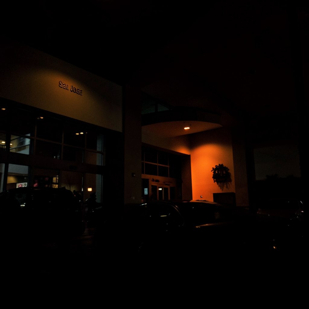 Dark, moody photograph of a hotel convention gathering space with dim lighting and deep shadows, evoking a quiet business atmosphere