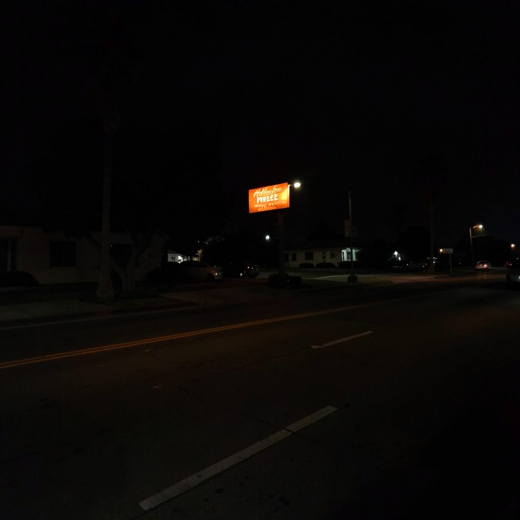 Low-lit photograph of a hotel exterior at twilight, soft beige and charcoal tones with deep shadows
